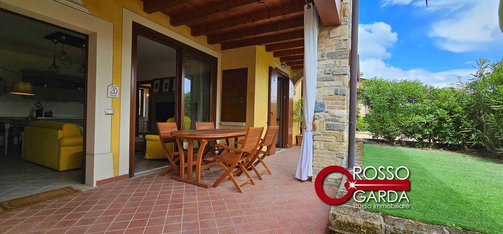 Appartamento piano terra con giardino e portico in Signorile Residence stile Sardegna in vendita a  Polpenazze del Garda